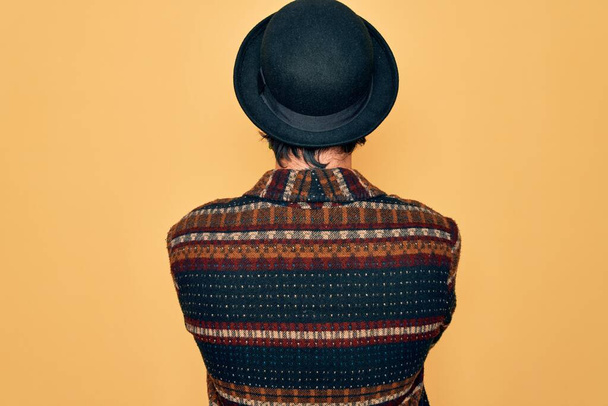 Joven hombre bohemio hispano guapo usando estilo hippie y sombrero boho de pie mirando hacia atrás con los brazos cruzados
 - Foto, Imagen