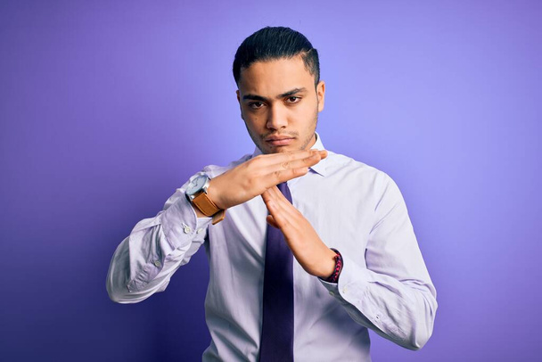 Молодой бразильский бизнесмен в элегантном галстуке стоит на изолированном фиолетовом фоне и делает жесты руками, расстроенное и серьезное лицо
 - Фото, изображение