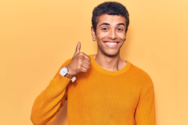 Νεαρός Αφροαμερικάνος που φοράει καθημερινά ρούχα χαμογελώντας χαρούμενος και θετικός, με τον αντίχειρα ψηλά και το σήμα έγκρισης  - Φωτογραφία, εικόνα