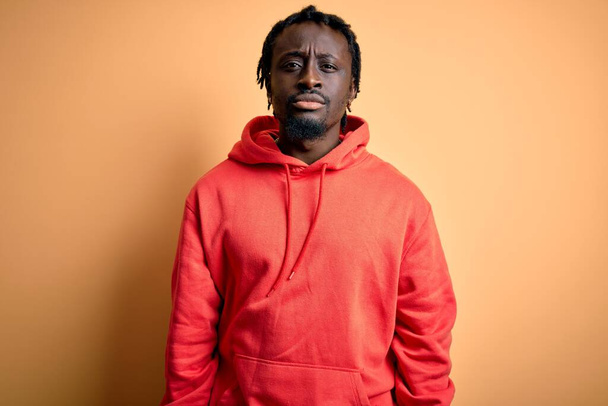 Young african american sporty man wearing sweatshirt with hoodie over yellow background Relaxed with serious expression on face. Simple and natural looking at the camera. - Photo, Image