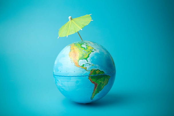 Η υπερθέρμανση του πλανήτη και η αλλαγή του κλίματος στη Γη. Γη σφαίρα σε μπλε φόντο με μια ομπρέλα. Προστασία της ατμόσφαιρας από την υπεριώδη ακτινοβολία και τις τρύπες του όζοντος - Φωτογραφία, εικόνα