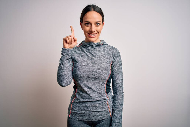 Fiatal szőke fitness nő visel sport edzőruha felett elszigetelt háttér mutatja, és rámutatva ujj első számú, miközben mosolygós magabiztos és boldog. - Fotó, kép