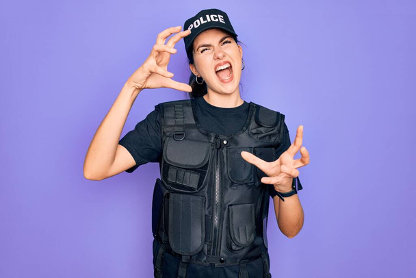 Young police woman wearing security bulletproof vest uniform over purple background Shouting frustrated with rage, hands trying to strangle, yelling mad - Photo, Image