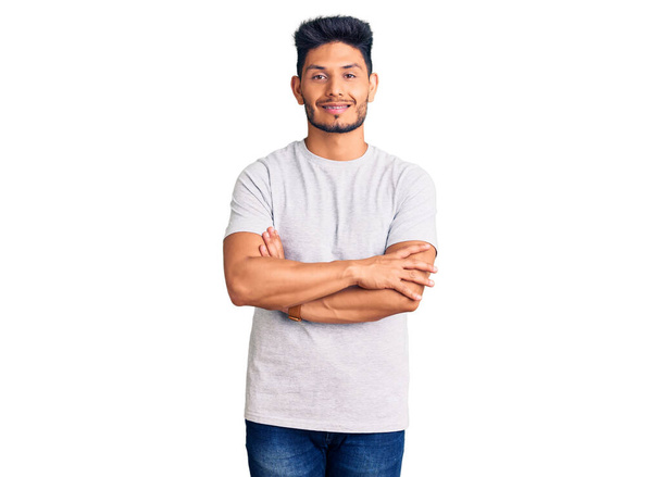 Jóképű latin-amerikai fiatalember alkalmi pólóban, boldog arccal, keresztbe tett karokkal, a kamerába nézve. pozitív személy.  - Fotó, kép