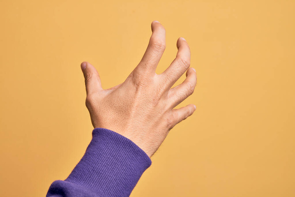 Main de jeune homme caucasien montrant les doigts sur fond jaune isolé saisissant agressif et effrayant avec les doigts, la violence et la frustration - Photo, image