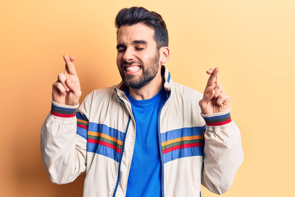 Young handsome man with beard wearing casual jacket gesturing finger crossed smiling with hope and eyes closed. luck and superstitious concept.  - Foto, Bild