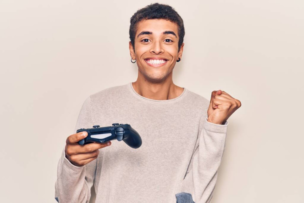 Молодий афроамериканський чоловік грає в відеогру, тримаючи контролер кричати гордо, святкуючи перемогу і успіх дуже схвильований піднятою рукою
  - Фото, зображення