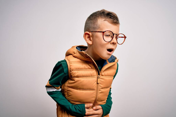 Young little caucasian kid with blue eyes wearing winter coat and smart glasses with hand on stomach because nausea, painful disease feeling unwell. Ache concept. - Фото, зображення