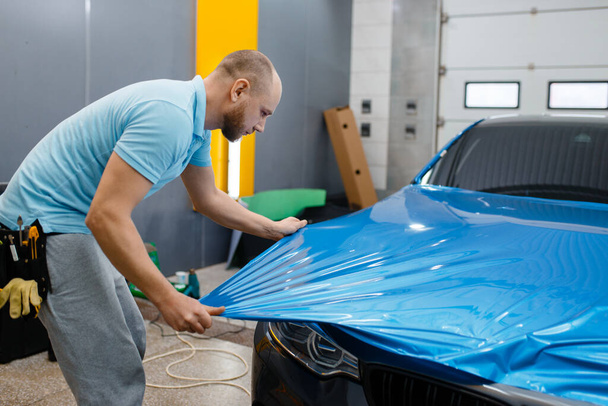 Male car wrapper puts protective vinyl foil or film on hood. Worker makes auto detailing. Automobile paint protection coating, professional tuning - Photo, Image