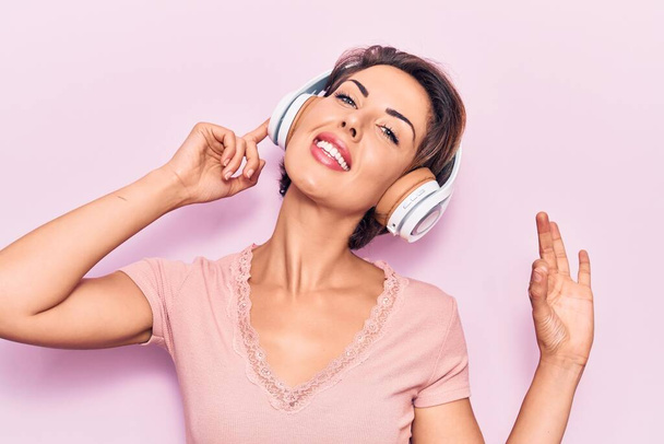 Joven hermosa mujer escuchando música usando auriculares haciendo signo de ok con los dedos, sonriendo gesto amistoso excelente símbolo  - Foto, imagen