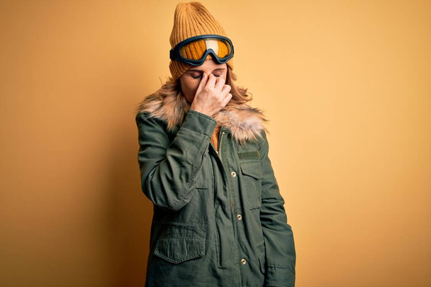 Середньовіччя красива блондинка лижниця в сніжному спортивному одязі і лижних окулярах втомилася розтирати ніс і очі, відчуваючи втому і головний біль. Концепція стресу та розчарування
. - Фото, зображення