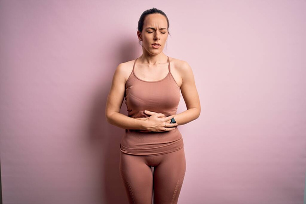 Joven mujer rubia fitness usando ropa de entrenamiento deportivo sobre fondo rosa aislado con la mano en el estómago porque la indigestión, la enfermedad dolorosa sensación de malestar. Concepto Ache
. - Foto, imagen