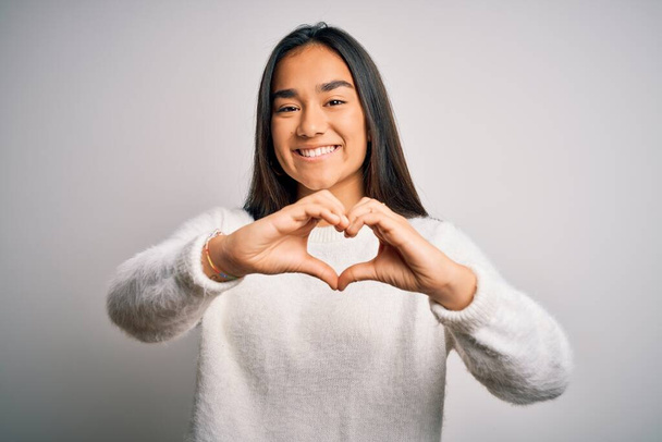 Young beautiful asian woman wearing casual sweater standing over white background smiling in love showing heart symbol and shape with hands. Romantic concept. - Photo, Image