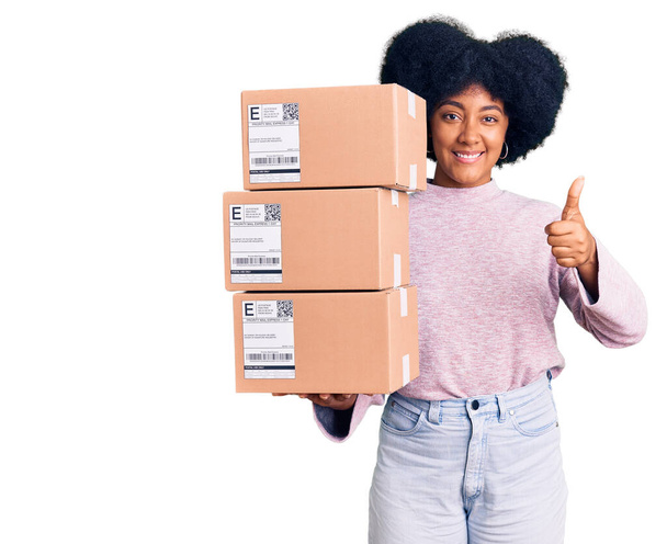Junge afrikanisch-amerikanische Mädchen mit Lieferung Paket lächelnd glücklich und positiv, Daumen hoch dabei hervorragende und Zustimmung Zeichen  - Foto, Bild