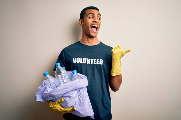 Красивий афро-американський волонтер переробляє пластикові пляшки, піклуючись про навколишнє середовище, вказуючи і показуючи великим пальцем в сторону з щасливим обличчям посміхаючись
 - Фото, зображення