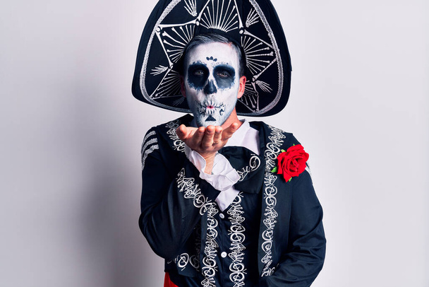 Jovem vestindo dia mexicano do traje morto sobre branco olhando para a câmera soprando um beijo com a mão no ar sendo adorável e sexy. expressão do amor
.  - Foto, Imagem