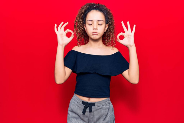 Beautiful kid girl with curly hair wearing casual clothes relax and smiling with eyes closed doing meditation gesture with fingers. yoga concept.  - Foto, Imagen
