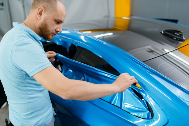 Car wrapping, mechanic cuts protective vinyl foil or film on vehicle. Worker makes auto detailing. Automobile paint protection coating, professional tuning - Photo, Image
