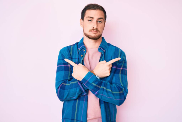 Mladý pohledný muž v neformálním oblečení ukazujícím prsty na obě strany, odlišný směr nesouhlasí  - Fotografie, Obrázek