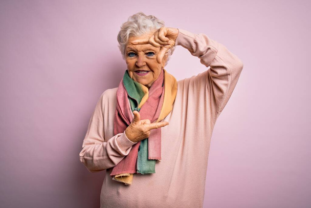 Starsza piękna siwowłosa kobieta ubrana w luźny sweter i szalik na różowym tle uśmiechnięta rama z dłońmi i palcami ze szczęśliwą twarzą. Koncepcja kreatywności i fotografii. - Zdjęcie, obraz