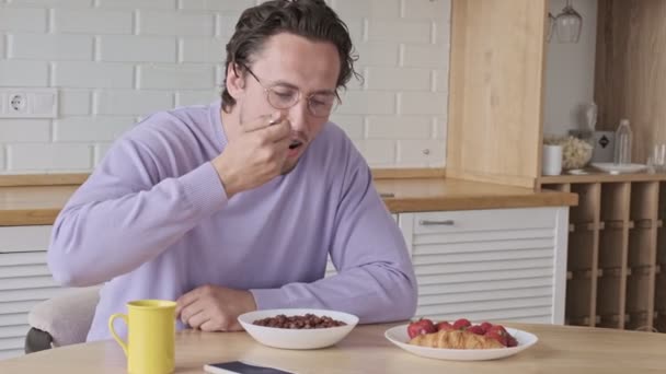Klidný pohledný muž v brýlích se snídaní u stolu doma - Záběry, video