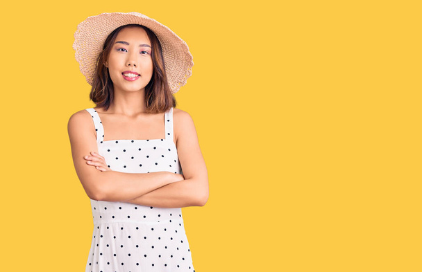 Jeune belle fille chinoise portant un chapeau d'été visage heureux souriant avec les bras croisés regardant la caméra. personne positive.  - Photo, image