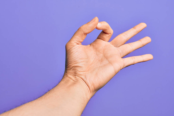 Hand of caucasian young man showing fingers over isolated purple background gesturing approval expression doing okay symbol with fingers - Photo, Image