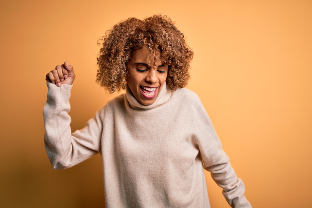 Молода африканська американка, одягнена в білизну светр над жовтим фоном Танці щасливі і веселі, усміхаючись, що рухається випадковим і впевнено слухає музику - Фото, зображення
