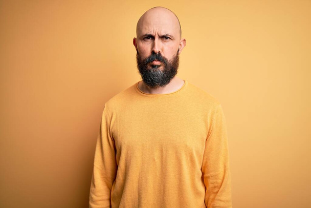 Handsome bald man with beard wearing casual sweater standing over yellow background depressed and worry for distress, crying angry and afraid. Sad expression. - Фото, изображение