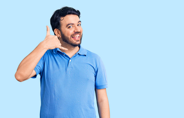 Young hispanic man wearing casual clothes smiling doing phone gesture with hand and fingers like talking on the telephone. communicating concepts.  - Foto, immagini