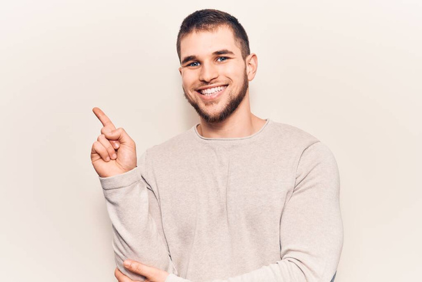 Joven hombre guapo usando suéter casual sonriendo feliz señalando con la mano y el dedo a un lado
  - Foto, Imagen