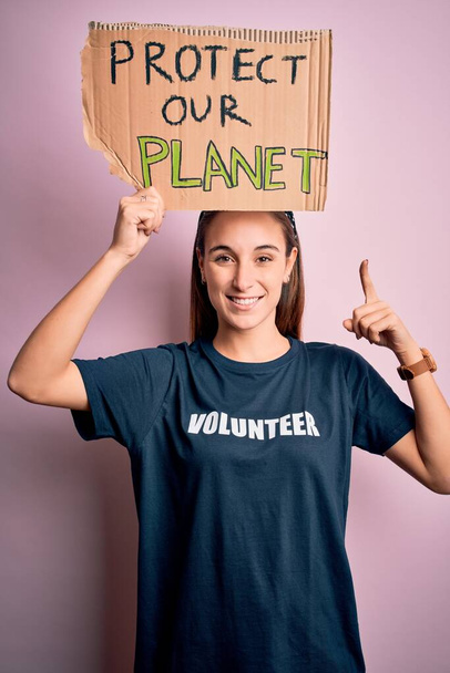 Beautiful volunteer woman doing volunteering holding banner with protect planet message very happy pointing with hand and finger - Foto, immagini
