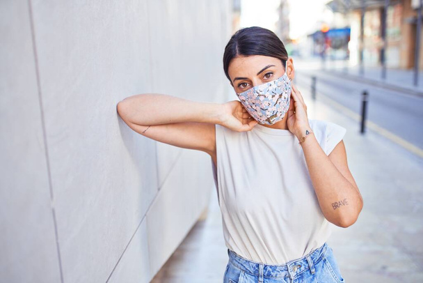 Hermosa mujer joven con ropa de moda y máscara de seguridad médica colorida para coronavirus caminando por la calle - Foto, imagen
