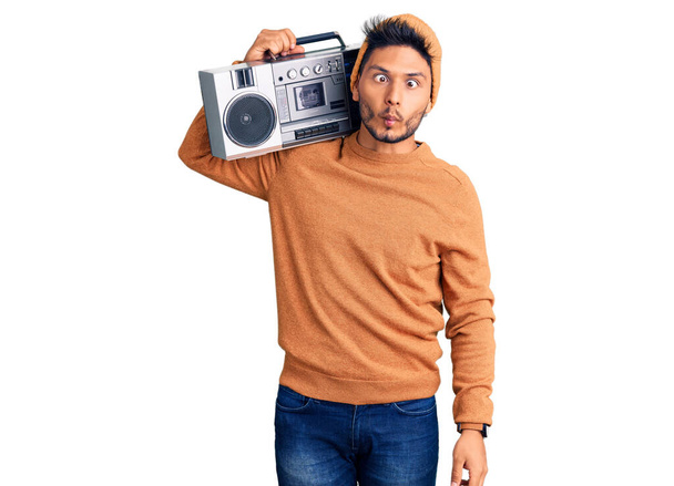 Handsome latin american young man holding boombox, listening to music making fish face with lips, crazy and comical gesture. funny expression.  - Foto, Imagem