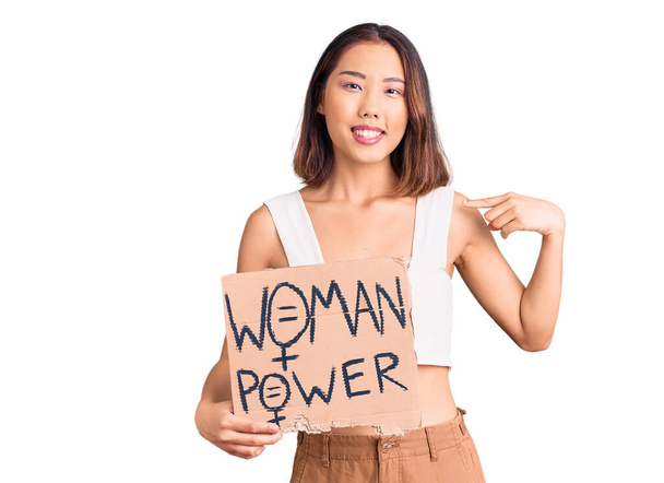 Young beautiful chinese girl holding woman power banner pointing finger to one self smiling happy and proud  - Photo, Image