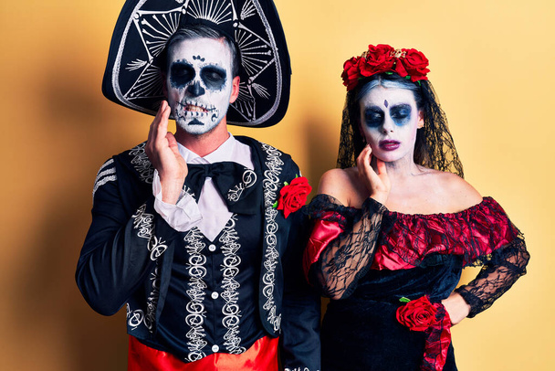 Young couple wearing mexican day of the dead costume over yellow touching mouth with hand with painful expression because of toothache or dental illness on teeth. dentist  - Fotografie, Obrázek