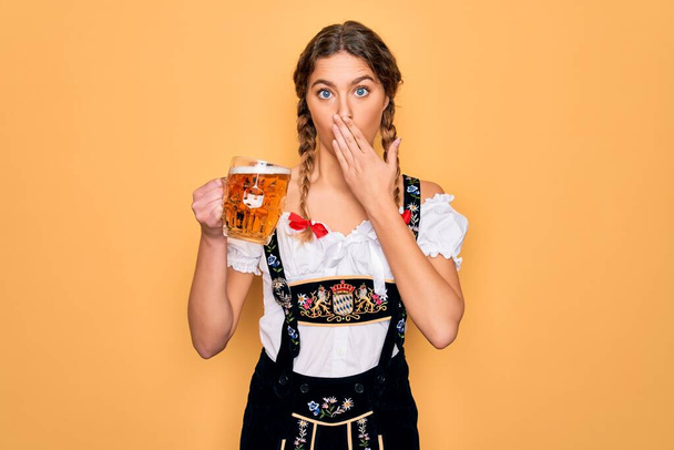 Beautiful blonde german woman with blue eyes wearing octoberfest dress drinking jar of beer cover mouth with hand shocked with shame for mistake, expression of fear, scared in silence, secret concept - 写真・画像