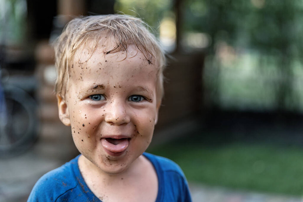 Милый очаровательный блондин белый маленький счастливый портрет мальчика-малыша с грязными пятнами муса на лице после игры полива сада на дворе или сельской ферме. Детское счастье летняя концепция страны
 - Фото, изображение