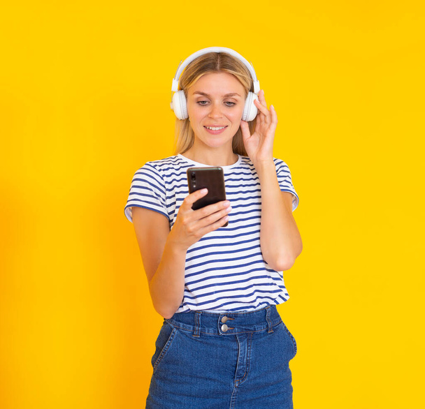 無制限の音楽アプリ。笑顔の女の子とともにヘッドフォンで音楽を聴く彼女の電話で黄色の背景 - 写真・画像