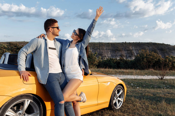 Happy young couple staying beside a yellow convertible car. Freedom, travel and love concept. - Фото, зображення