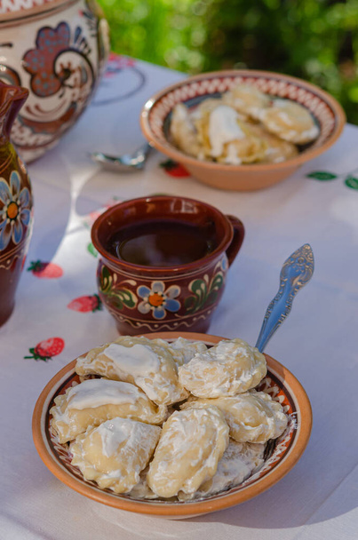Pierogi fatti in casa in argilla piatti etnici ucraini su un tavolo nel giardino estivo. Cucina nazionale, stile di vita - Foto, immagini