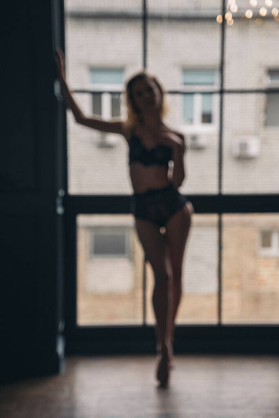 Unfocused bokeh image. Gorgeous sexy slim woman in underwear. She wear seductive lingerie and pose sensually in dark rich interior. Portraits with dim backlight and dark, deep shadows. Copy Space - Zdjęcie, obraz