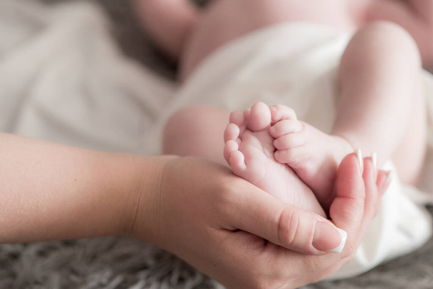 Maternal hands hold baby legs on the bed at home. Happy and healthy motherhood. Child care - Φωτογραφία, εικόνα