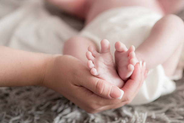 Maternal hands hold baby legs on the bed at home. Happy and healthy motherhood. Child care - Φωτογραφία, εικόνα