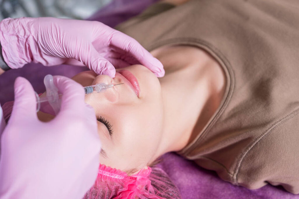 Врач-косметолог делает инъекции женщине в клинике. Она носит светящиеся и маски и держит шприц с иглой. - Фото, изображение