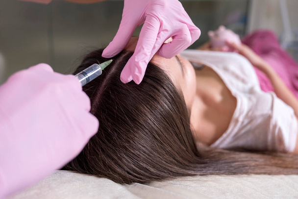 Kosmetologe Arzt machen Injektionsverfahren zu einer Frau in ihrer Klinik. Sie trägt rosa Handschuhe und Maske und hält Spritze mit Nadel. - Foto, Bild