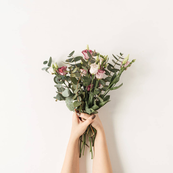 Female hands holding colorful roses flowers bouquet against white wall. Holiday celebration festive floral concept - Foto, afbeelding