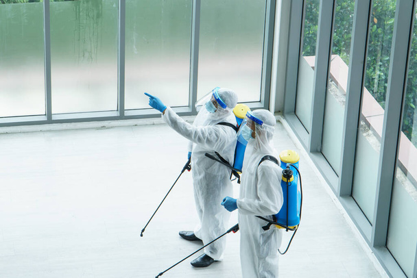 Profesjonalny pracownik W odzieży ochronnej i maskach rozpylają środki dezynfekujące, czyszczące, kontrolujące wirusa i bakterie w zanieczyszczonym obszarze Po rozprzestrzenianiu się koronawirusu lub COVID-19 - Zdjęcie, obraz