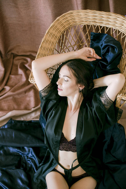 Young attractive girl with dark hair in a black silk robe in a boudoir setting. Beauty and Fashion - 写真・画像