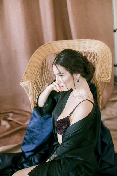 Young attractive girl with dark hair in a black silk robe in a boudoir setting. Beauty and Fashion - Fotó, kép